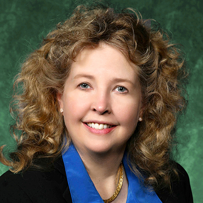 A headshot of Angela Wilson smiling wearing a black blazer over a blue dress shirt with a gold necklace