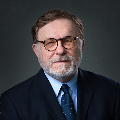 A headshot of Borys Hrinczenko smiling wearing glasses with a black blazer over a blue dress shirt and tie