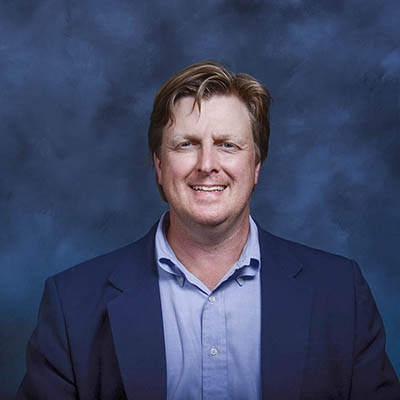 A headshot of Brian Petroff smiling wearing a black blazer over a blue dress shirt