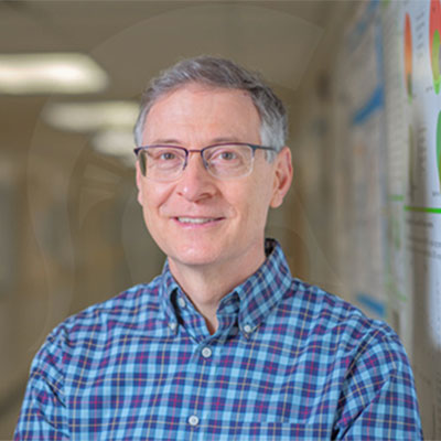 A headshot of David Arnosti smiling wearing a blue plaid button up and glasses