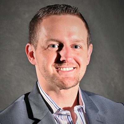 A headshot of David Hickey smiling wearing a gray blazer over a colorful striped dress shirt