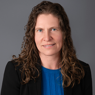 A headshot of Jennifer Jacob smiling wearing a black blazer over a blue shirt