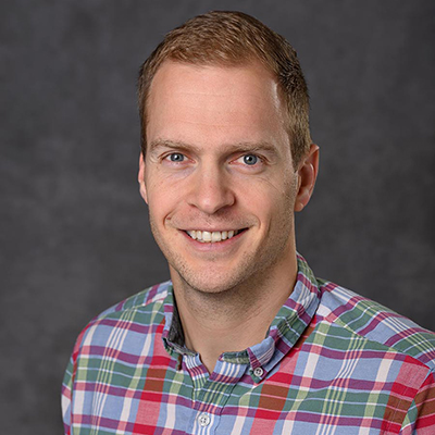 A headshot of Jens Schmidt smiling wearing a plaid shirt
