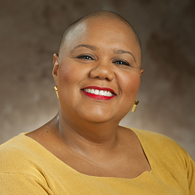 A headshot of Karen Kelly-Blake smiling wearing a yellow top