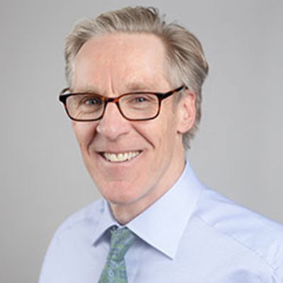 A headshot of Mat Reeves smiling wearing glasses and a blue dress shirt and tie