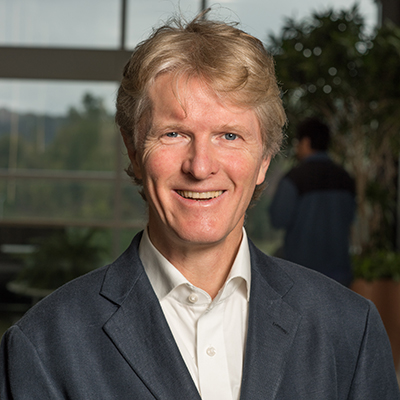 A headshot of Micheal Bachmann in a black and white suit smiling