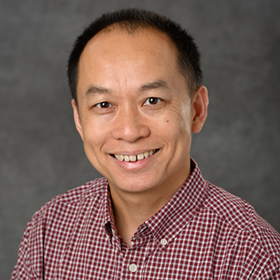 A headshot of Ming Chen smiling while wearing a red and white checkered button up polo