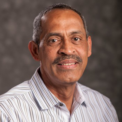 A headshot of Muraleedharan Nair smiling wearing a white striped dress shirt
