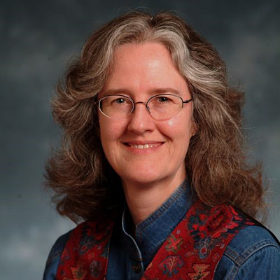 A headshot of Nancy Turner wearing glasses smiling while wearing a jean top and red scarf