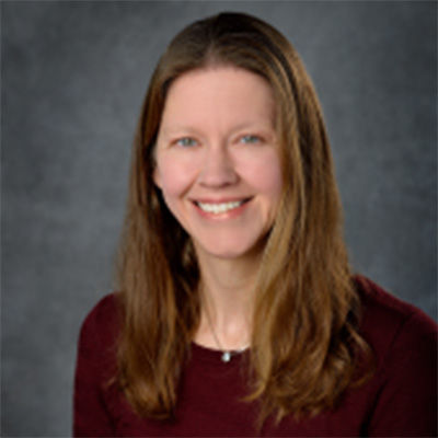 A headshot of Rebecca Smedley smiling wearing a burgundy top and necklace 