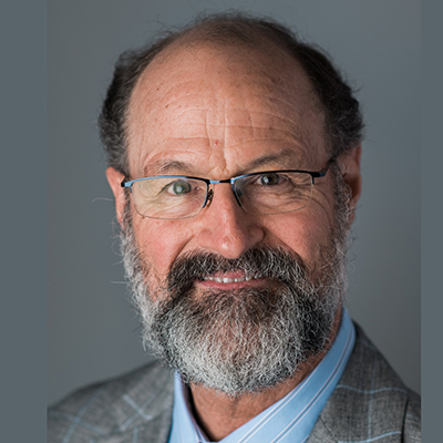 A headshot of Richard Neubig smiling wearing glasses and a gray blazer over a blue dress shirt