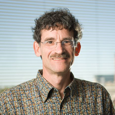 A headshot of Richard Schwartz smiling wearing glasses with a colorful dress shirt
