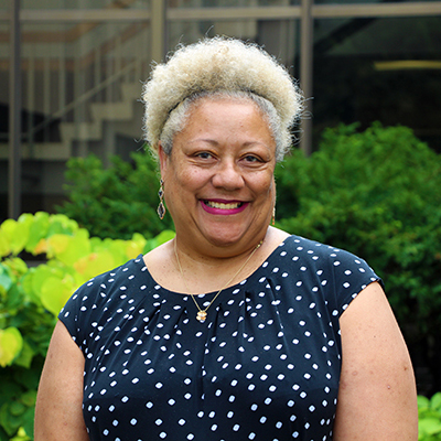 A headshot of Sabrina Ford smiling outside while wearing a blue and white polka dot top