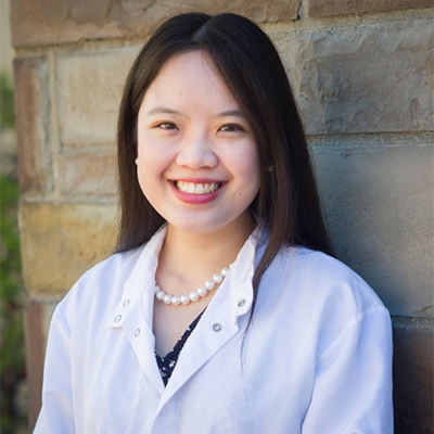 A headshot of Sachi Horibata smiling wearing a white lab coat with a pearl necklace