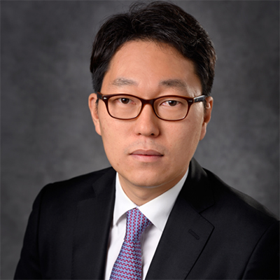 A headshot of Taeho Kim wearing glasses with a black blazer over a white dress shirt and purple tie