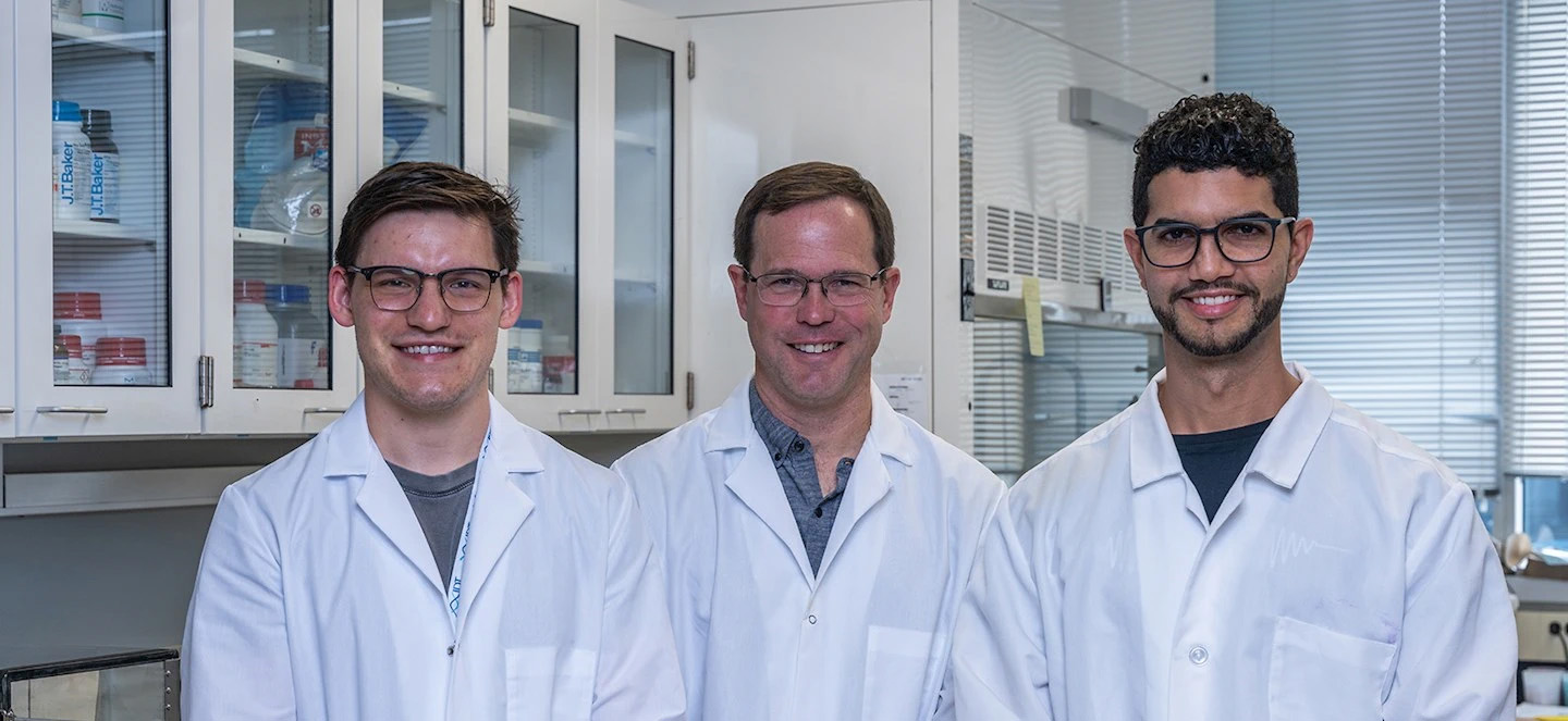 Three people wearing lab coats posing and smiling