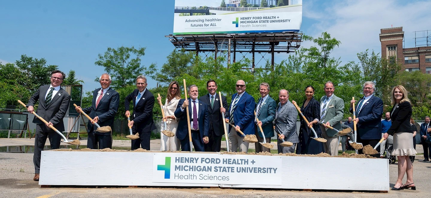 Group posing with shovels by a Henry Ford Health + Michigan State University Health Sciences sign