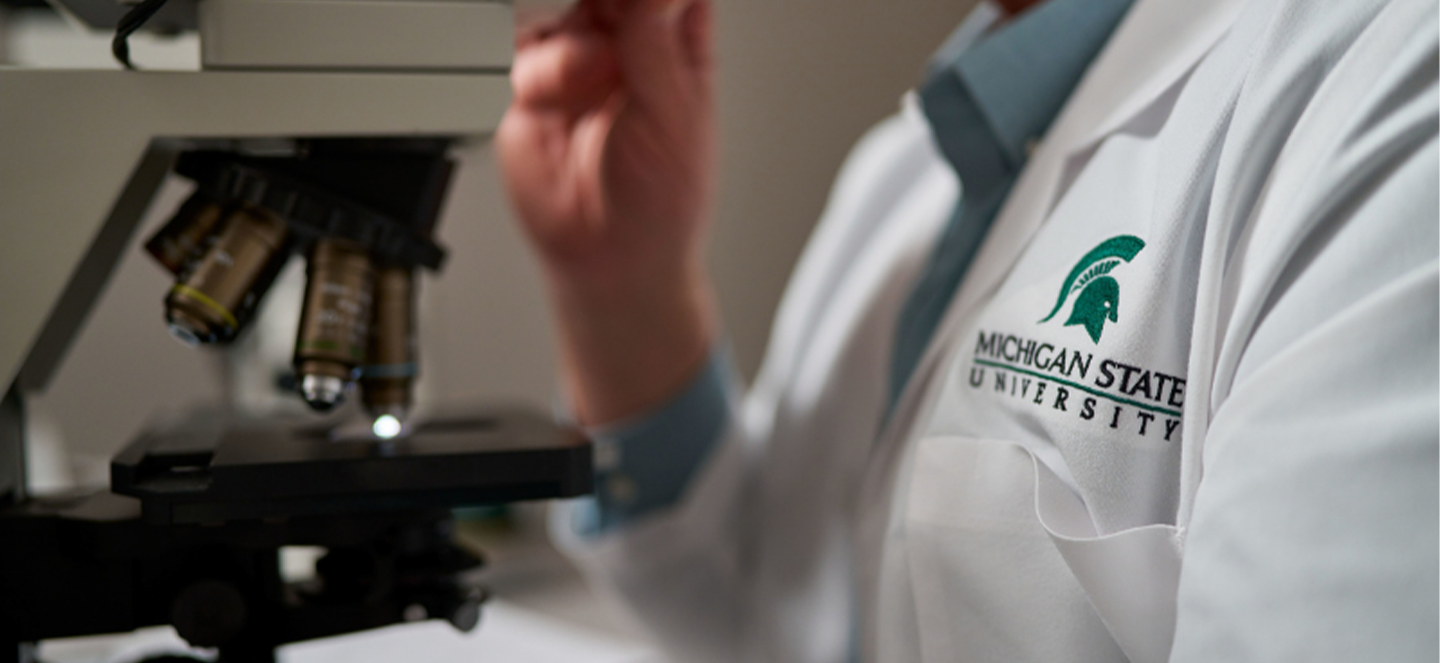 A person in a white coat operating a microscope