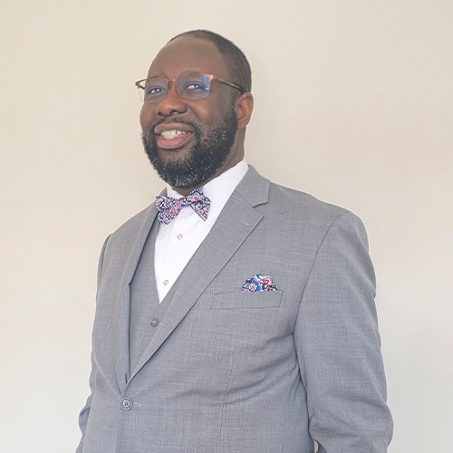 A headshot of Olorunseun Ogunwobi wearing glasses and a gray suit. 