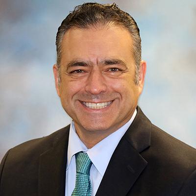 A headshot of Andrea Amalfitano smiling while wearing a black suit with a blue tie 