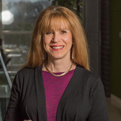 A headshot of Anna Moore smiling wearing a black blazer over a purple top