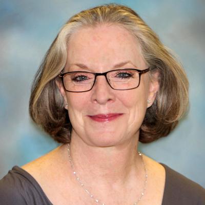 A headshot of Barbara Luke smiling wearing glasses and a gray top