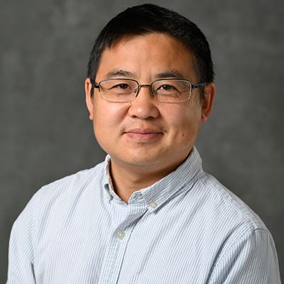 A headshot of Bin Chen smiling while wearing a white and blue polo button up with glasses