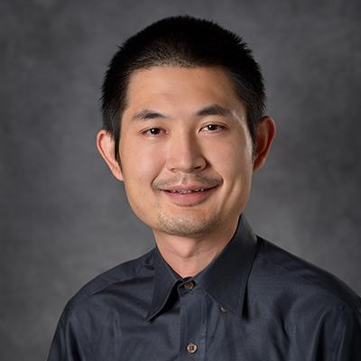 A headshot of Bin Gu smiling in a black dress shirt