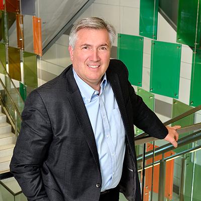 A photo of Christopher Contag smiling in a suit while posing in a stair well