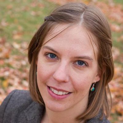 A phot of Courtney Carignan smiling in a gray blazer standing outside with leaves on the floor
