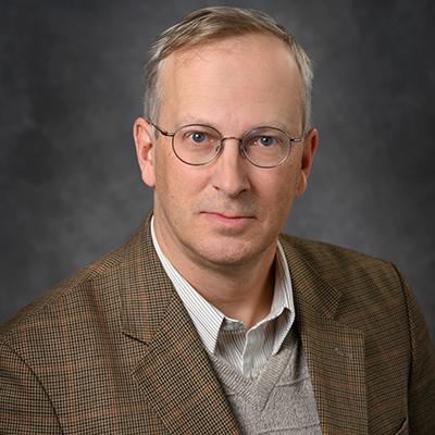 A headshot of Dalen Agnew in a suit wearing glasses