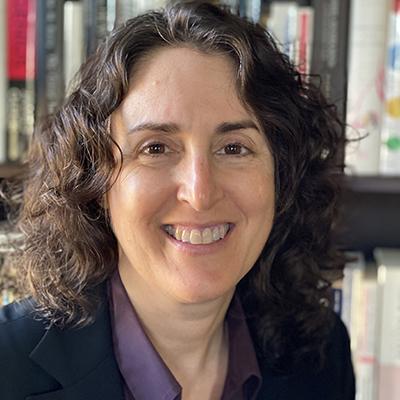 A headshot of Dawn Misra smiling wearing a black blazer over a purple dress shirt