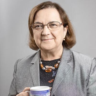 A headshot of Dorothy Pathak smiling wearing glasses with a gray blazer over a black dress shirt