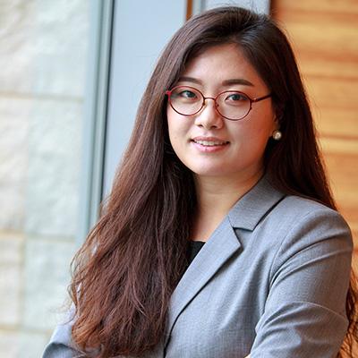 A headshot of Eunhee Yi smiling wearing red glasses and a gray blazer over a black shirt