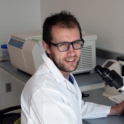 A headshot of Geoffroy Laumet smiling wearing glasses working in a lab with a white lab coat