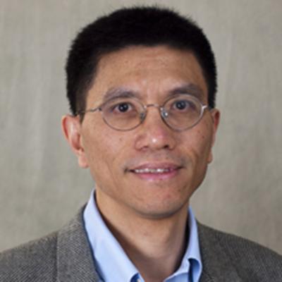 A headshot of Hua Xiao smiling wearing glasses and a gray blazer over a blue dress shirt