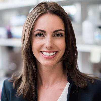 A headshot of Jamie Bernard smiling for a headshot wearing a black blazer with a white blouse
