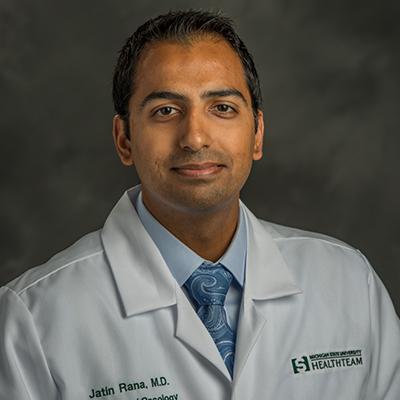 A headshot of Jatin Rana smiling wearing a white lab coat over a blue dress shirt and tie