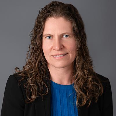 A headshot of Jennifer Jacob smiling wearing a black blazer over a blue shirt