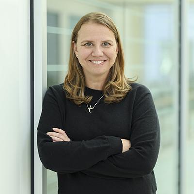 A headshot of Jennifer Klmo smiling crossing her arms wearing a black long sleeve top