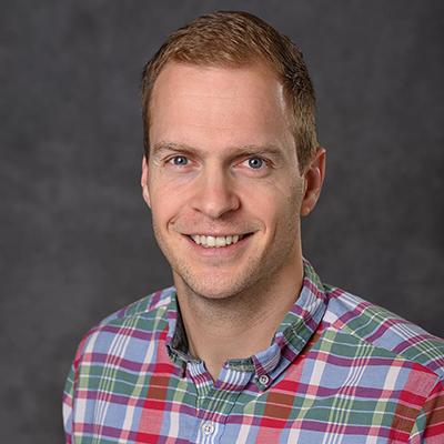 A headshot of Jens Schmidt smiling wearing a plaid shirt