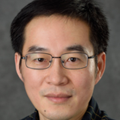 A headshot of Jin He smiling and wearing glasses and a black top