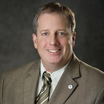A headshot of John Risinger smiling wearing a suit and tie