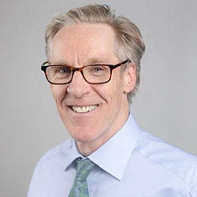 A headshot of Mat Reeves smiling wearing glasses and a blue dress shirt and tie