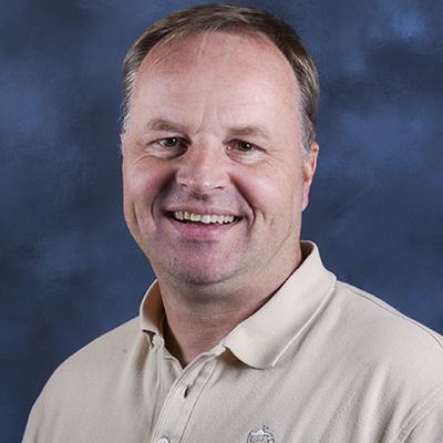 A headshot of Matti Kiupel smiling wearing a tan dress shirt