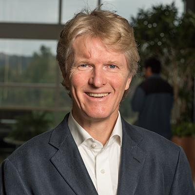 A headshot of Micheal Bachmann in a black and white suit smiling