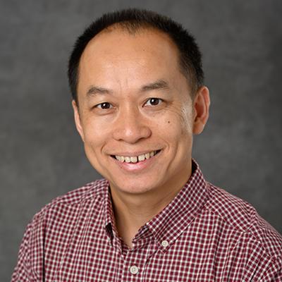 A headshot of Ming Chen smiling while wearing a red and white checkered button up polo
