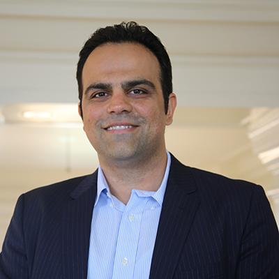 A headshot of Morteza Mahmoudi smiling wearing a black blazer over a blue dress shirt