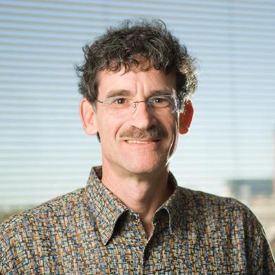 A headshot of Richard Schwartz smiling wearing glasses with a colorful dress shirt