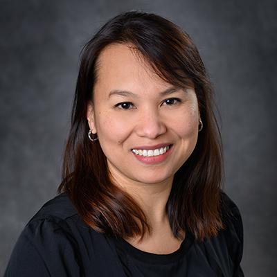 A headshot of Tuddow Thaiwong smiling wearing a black top and silver hoop earrings